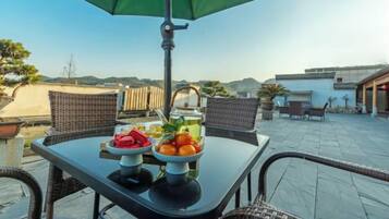 An outdoor patio with wicker chairs, a table with a green umbrella, and a bowl of fruit.