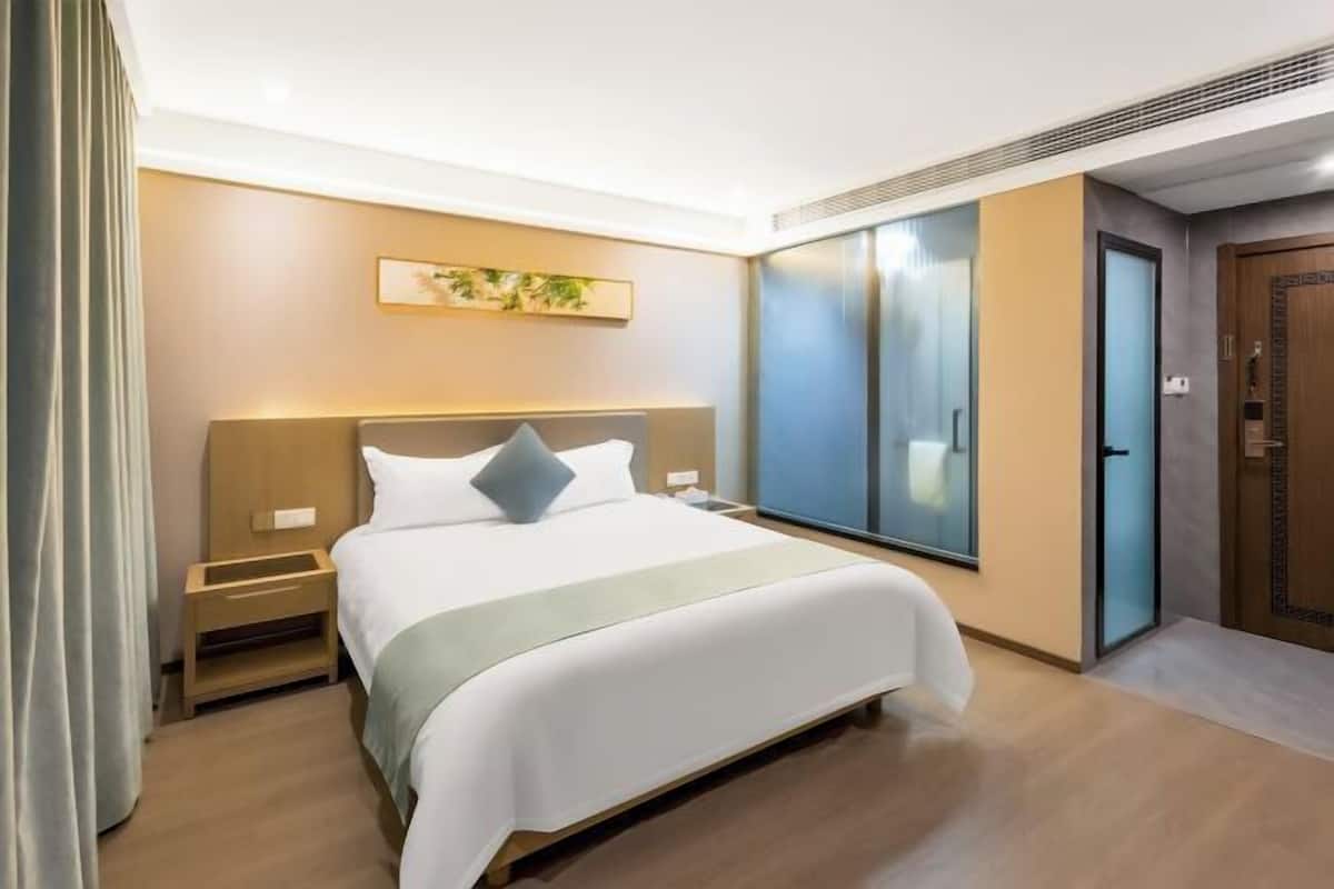 A hotel room with a large bed, a nightstand, a bedside table, a window, and a door.