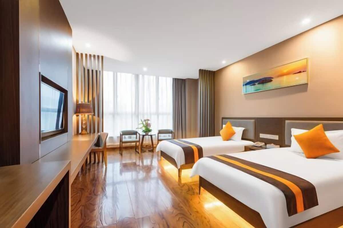 A hotel room with two beds, a desk, a chair, a TV, and a painting on the wall.