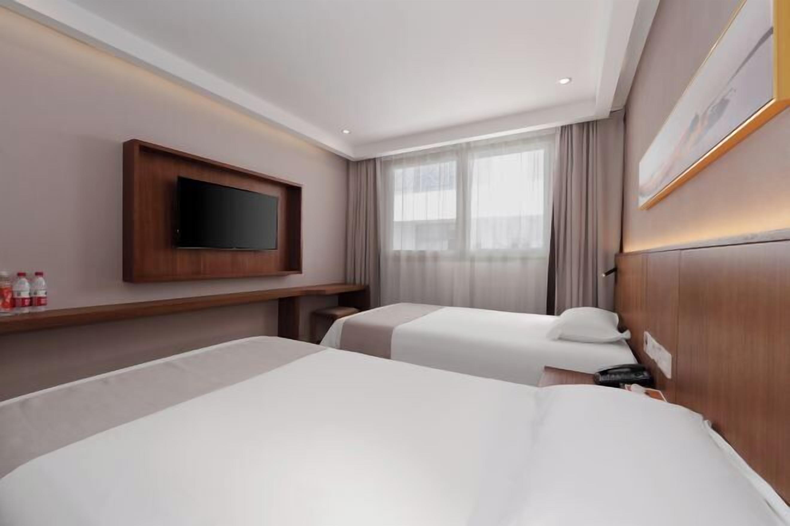 Une chambre d’hôtel avec deux lits, un téléviseur fixé au mur, une fenêtre avec des rideaux et une table de chevet avec un téléphone.