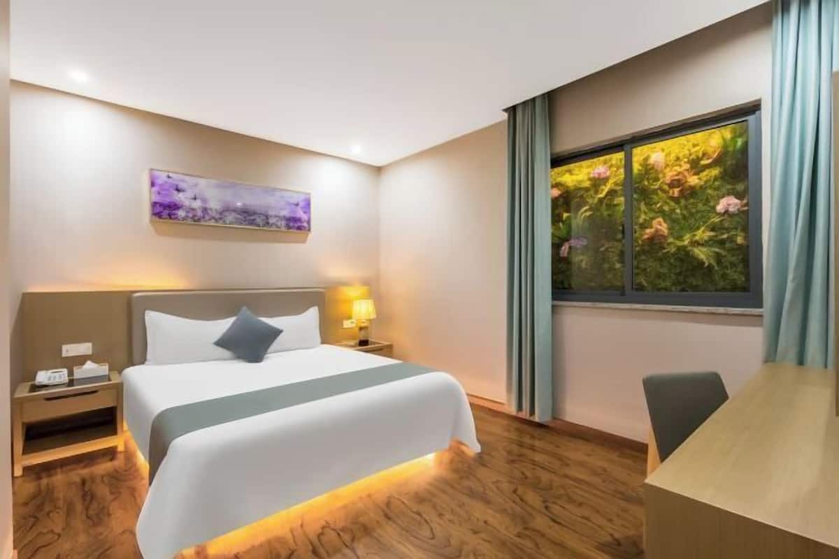 A hotel room with a bed, bedside table, lamp, and a window with curtains.