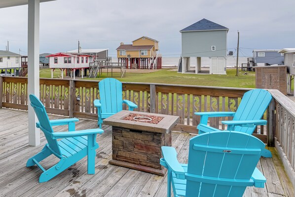 Une terrasse en bois avec des fauteuils Adirondack turquoise et une table de feu en pierre.