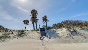 Ein Sandstrand mit Palmen und einer Treppe, die nach oben führt.