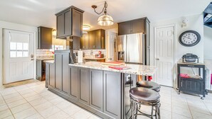 A modern kitchen with dark cabinets, a large island with stools, a stainless steel refrigerator, and a clock on the wall. - 8 Mi to Tellico Plains: Family Home Near Trails! (Englewood)