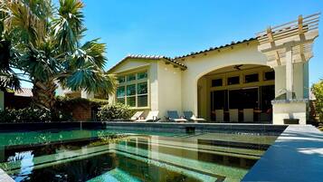 A poolside area with a clear pool, lounge chairs, and a building with large windows and a pergola.