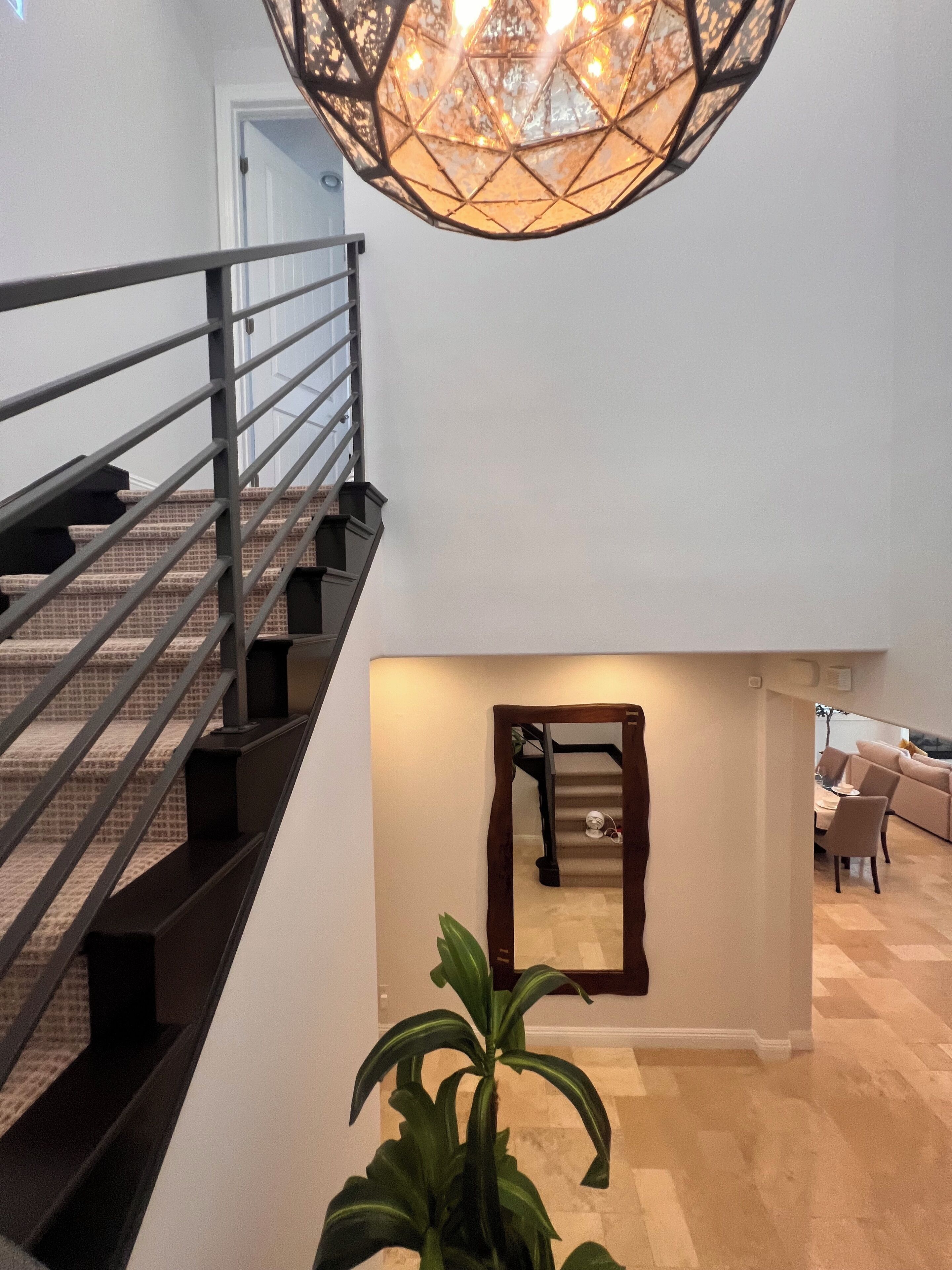 A staircase with a metal railing leading to a landing. A potted plant is in the foreground.