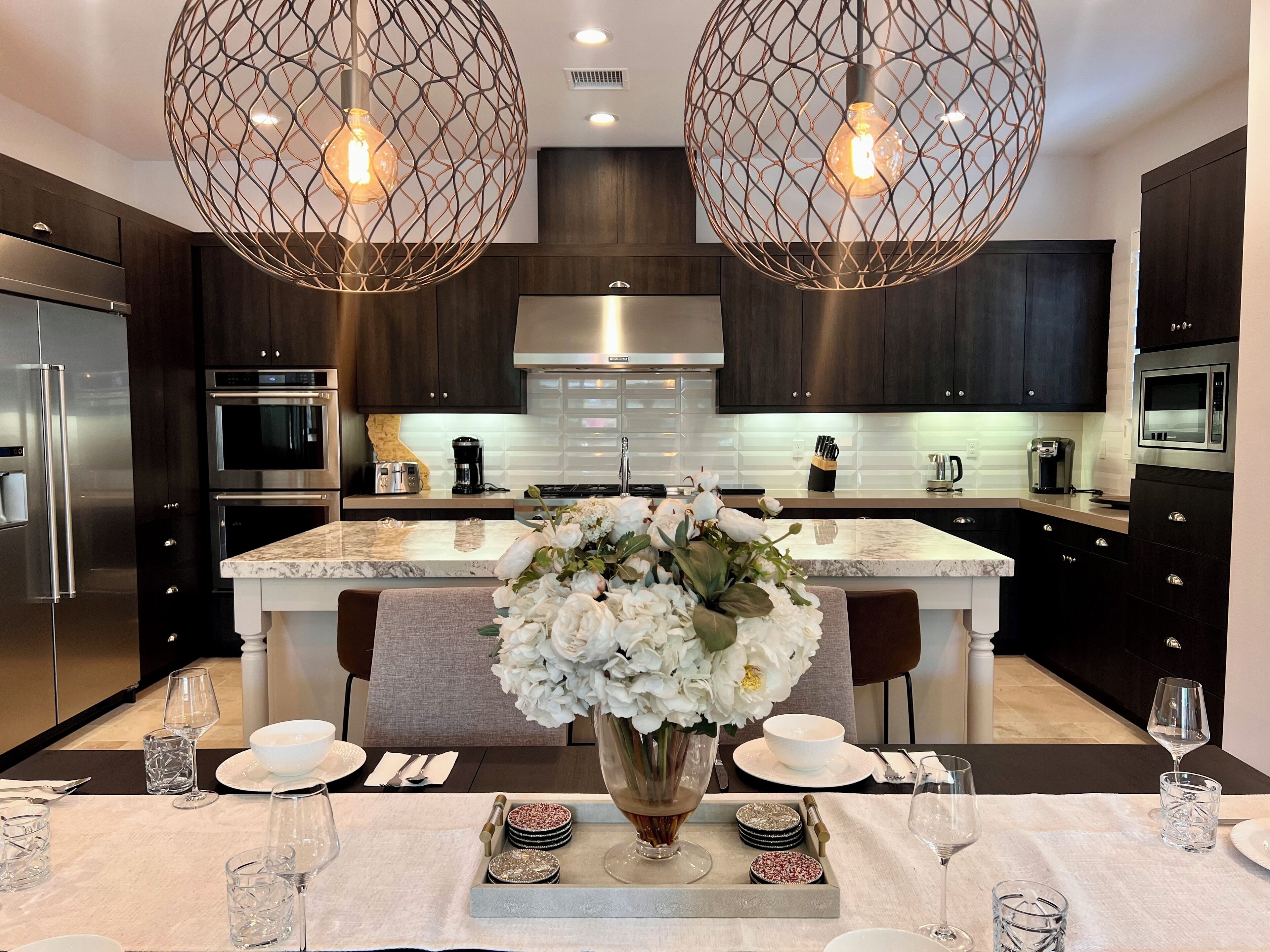 A modern kitchen with dark cabinetry, stainless steel appliances, and a marble island.