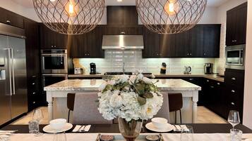 A modern kitchen with dark cabinetry, stainless steel appliances, and a marble island.