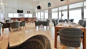 Een ruime eetruimte met hoge plafonds, plafondventilatoren en grote ramen met uitzicht op zee.
