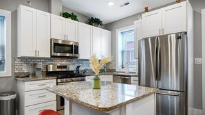 A modern kitchen with white cabinets, stainless steel appliances, granite countertops, and red bar stools. - Bright Washington DC Apartment (Washington)
