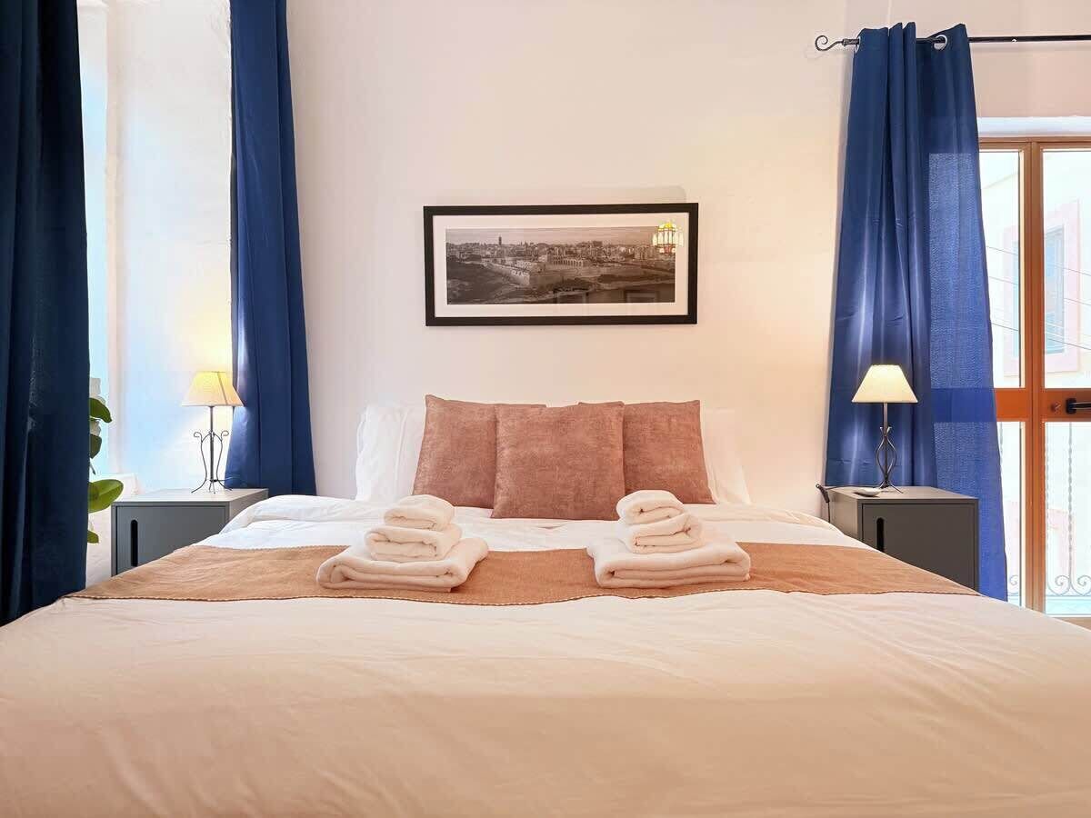 Una camera d'albergo con un letto, due cuscini, un quadro appeso alla parete e una finestra con tende.