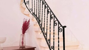Eine Treppe mit schwarzer Metallreling und ein Blumenvasen mit roten Blumen auf einer Holzkommode.