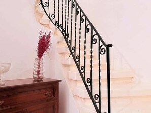 A staircase with a black metal railing and a vase with red flowers on a wooden dresser.