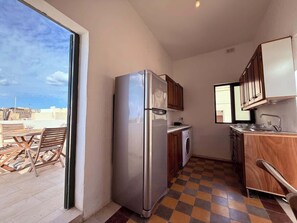 A compact kitchen with a refrigerator, washing machine, and wooden cabinets.