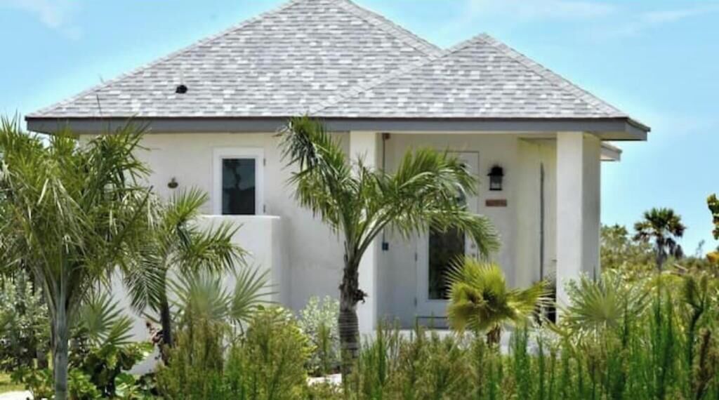 Une maison de plain-pied, dotée d’un toit recouvert de tuiles grises et entourée d’une végétation tropicale.