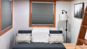 A compact room with a bunk bed, a sofa, a floor lamp, and a wooden ladder. - Secluded Tiny Cabin with firepit, stargaze and hike (Paige)