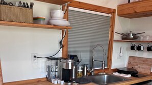 A compact kitchen with a wooden countertop, stainless steel appliances, and a small trash bin. - Secluded Tiny Cabin with firepit, stargaze and hike (Paige)