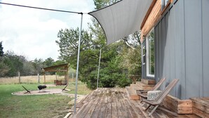 A wooden deck with outdoor furniture, a pergola, and a large shade sail. - Secluded Tiny Cabin with firepit, stargaze and hike (Paige)