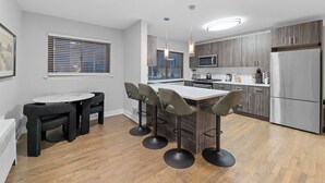 Una cocina moderna con una isla central, taburetes de bar, una mesa de comedor y electrodomésticos integrados.