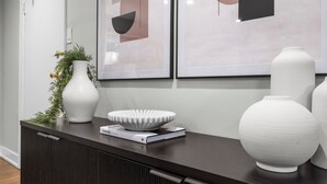 Un interior moderno con una consola de madera oscura, un jarrón blanco, un cuenco decorativo y arte abstracto enmarcados en la pared.