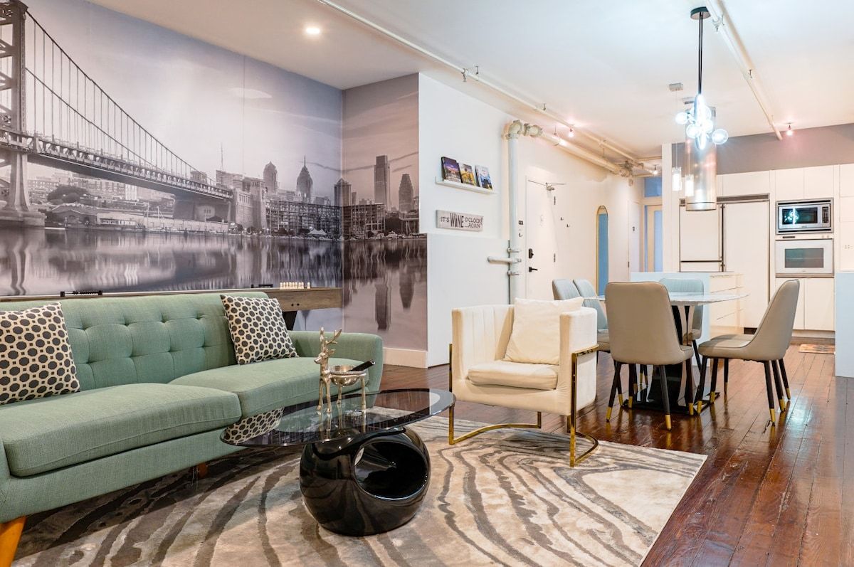 A modern living room with a green sofa, a glass coffee table, and a cityscape mural on the wall.