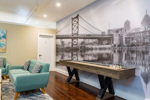 A room with a large wall mural of a bridge, a pool table, and a teal sofa. - Old City 2BR Apt w/ Shuffleboard! Walk Everywhere! (Philadelphia)