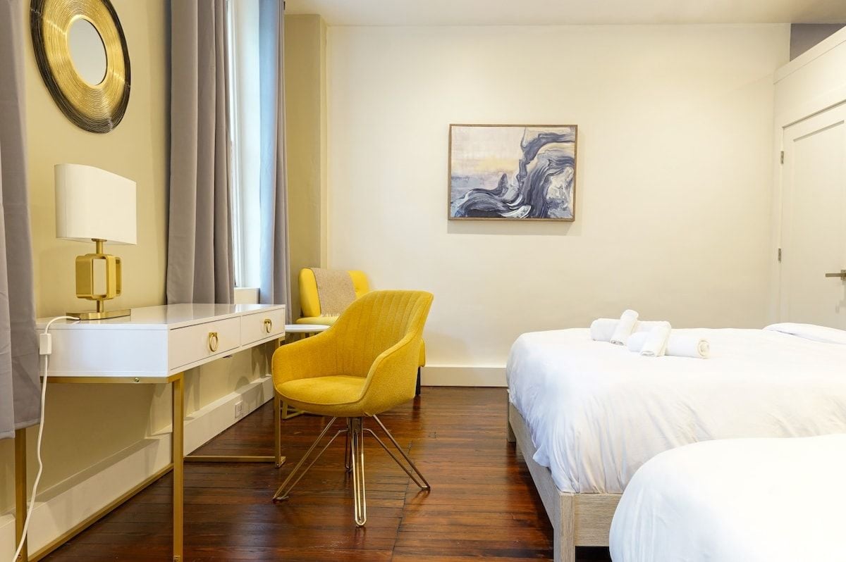 A hotel room with a bed, a desk with a lamp, a chair, and a painting on the wall.