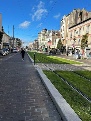 Ένα πεζοδρόμιο που διατρέχει παράλληλα τις γραμμές του τραμ, με κτίρια και στις δύο πλευρές και έναν καθαρό ουρανό.