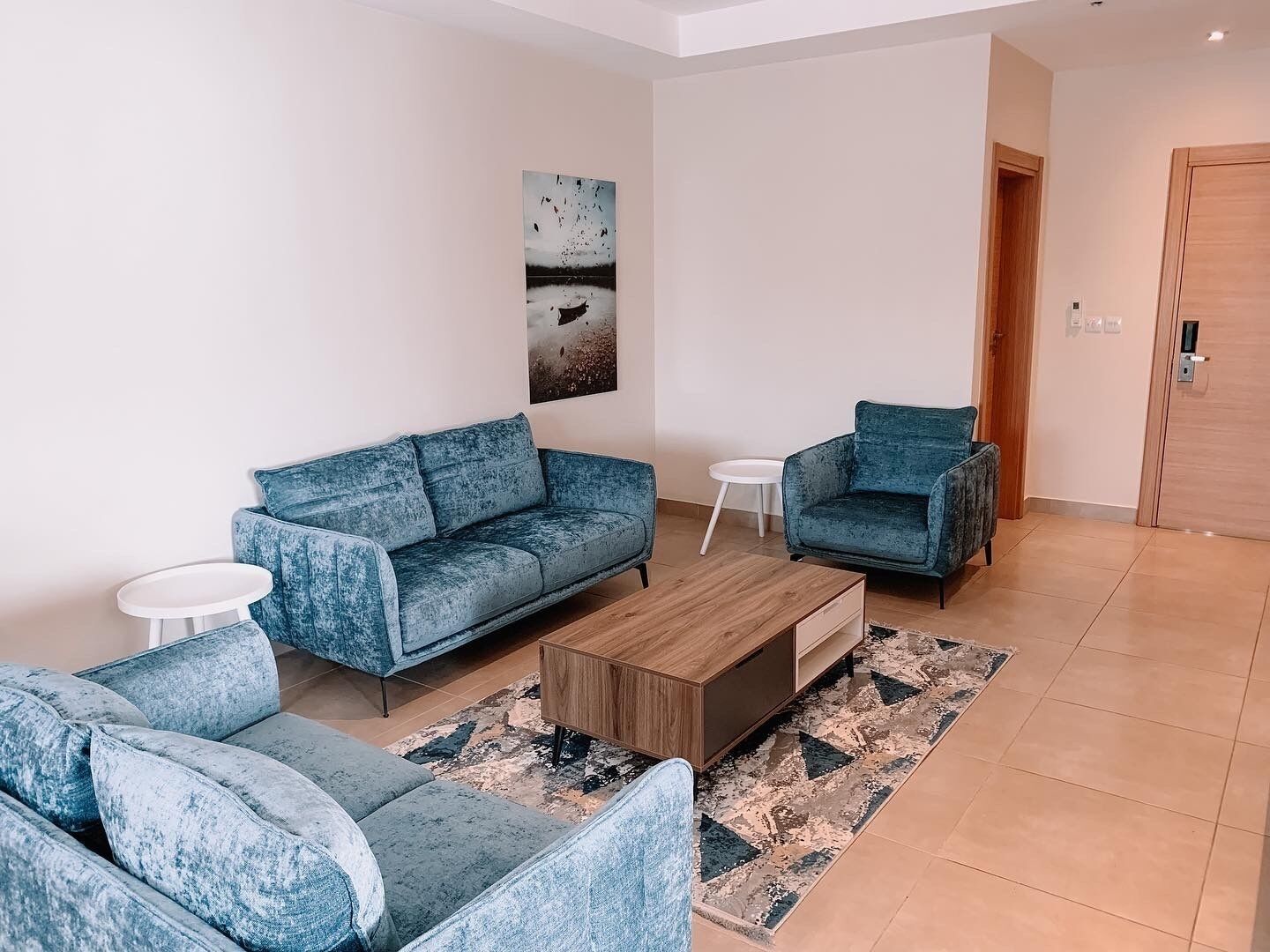 A modern living room with a blue sofa set, a wooden coffee table, and a small side table.