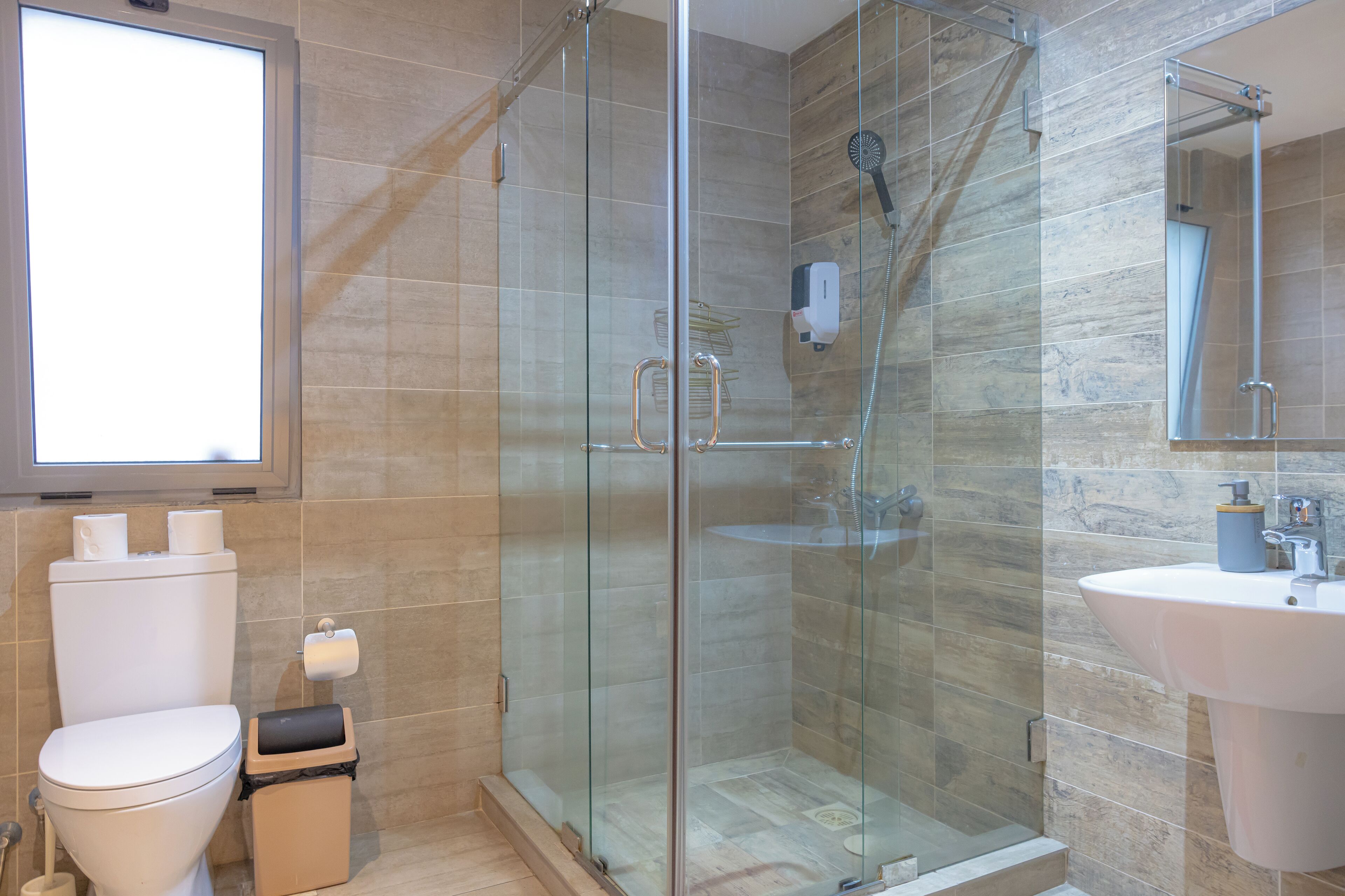 A modern bathroom with a glass-enclosed shower, a toilet, and a sink.