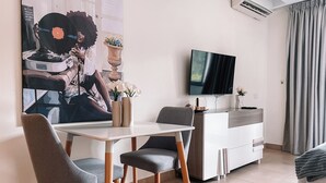 A modern living room with a dining area, a flat-screen TV mounted on the wall, and a large painting on the wall. - Sky Suites Airport (Accra)
