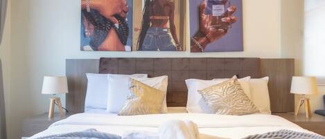 A hotel room with a large bed, two bedside tables, and three wall-mounted artworks.