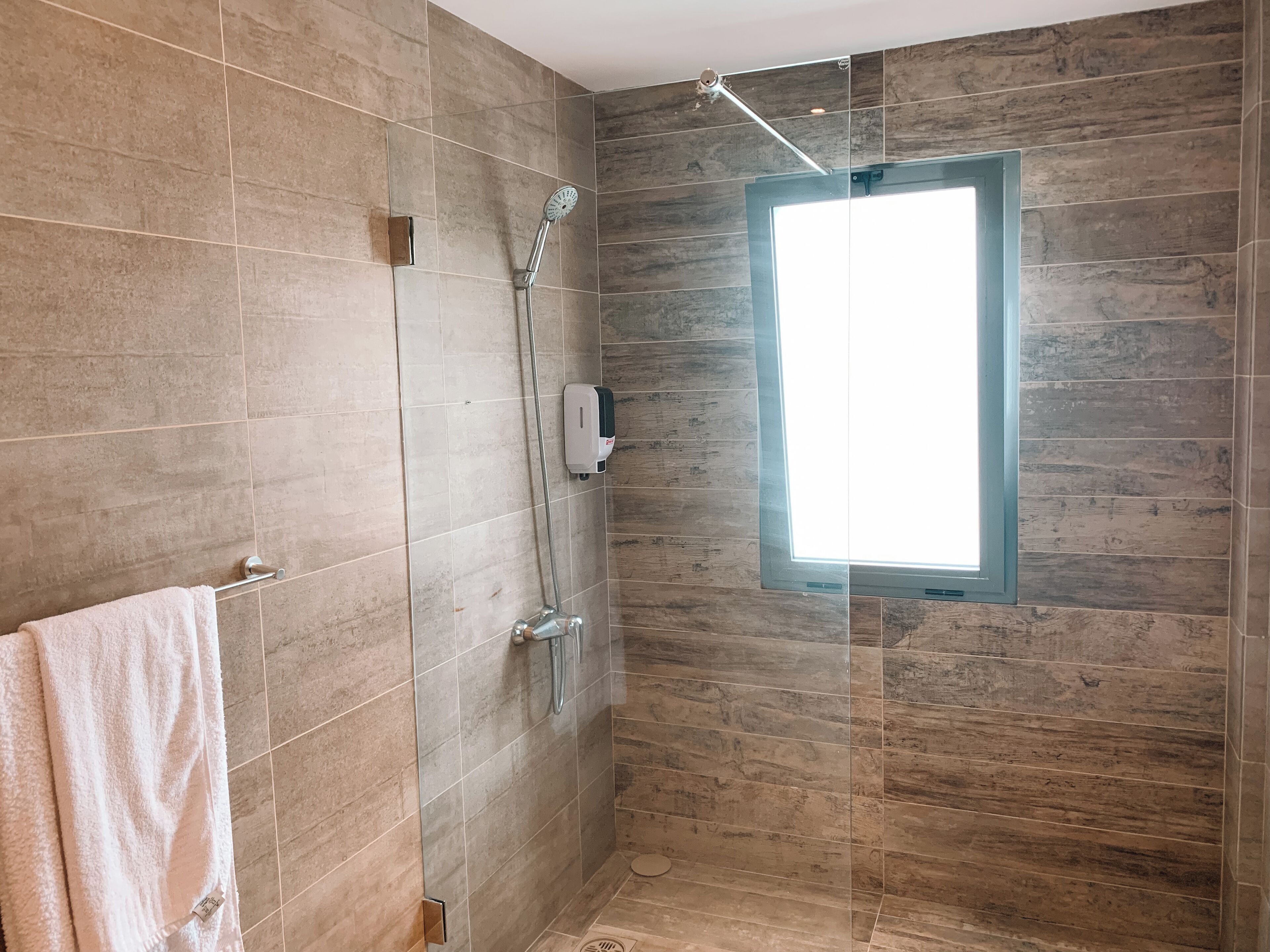 Un baño moderno con ducha de vidrio, un perchero con una toalla blanca y una ventana que proporciona luz natural.