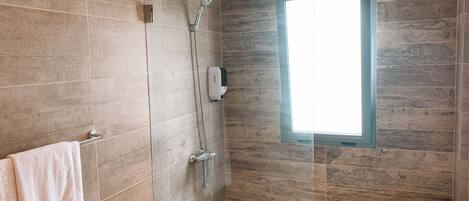 Un baño moderno con ducha de vidrio, un perchero con una toalla blanca y una ventana que proporciona luz natural.