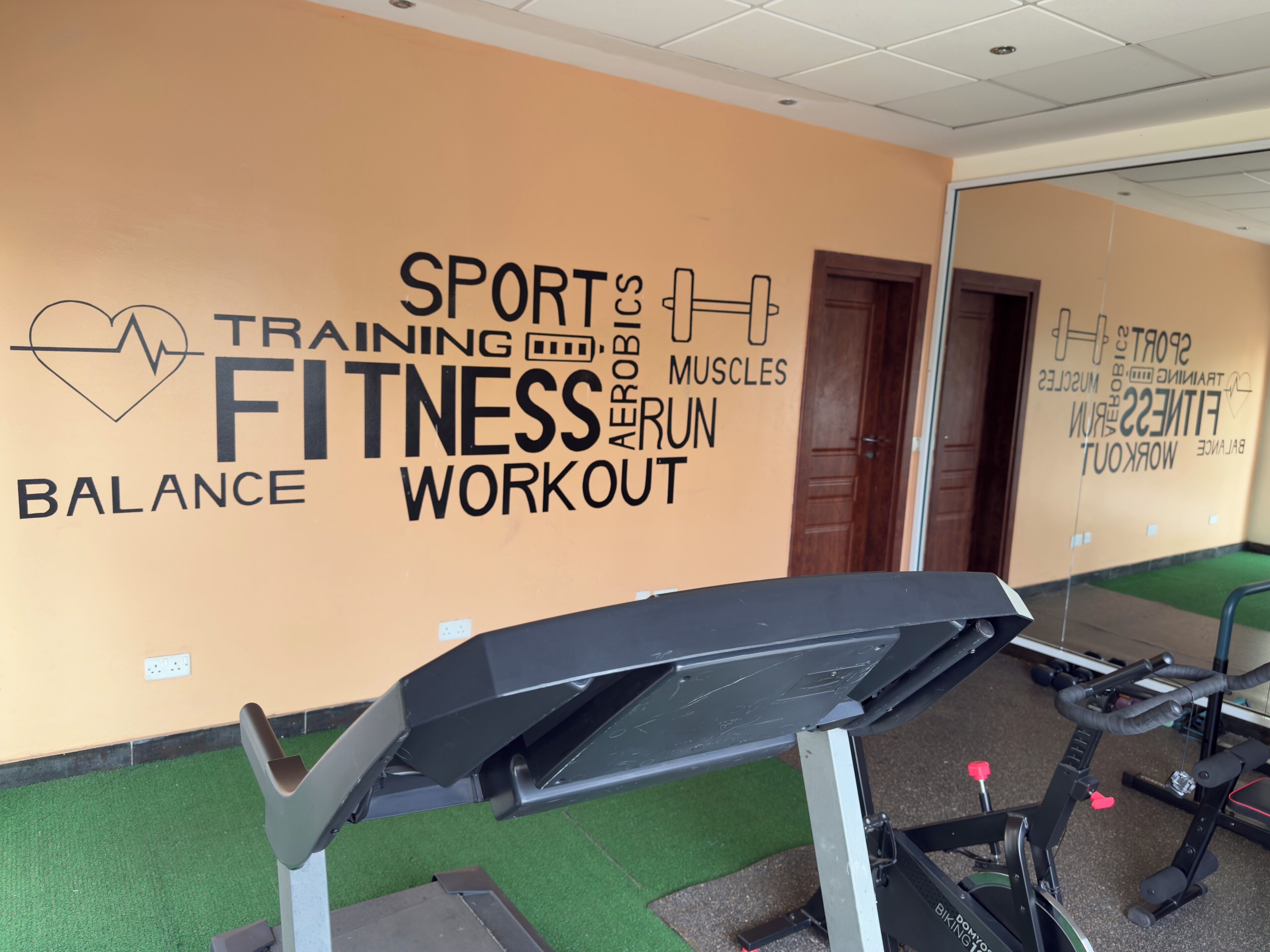 Een sportschool met een muur waarop woorden staan zoals 'SPORT', 'FITNESS', 'BALANS' en 'WORKOUT'.