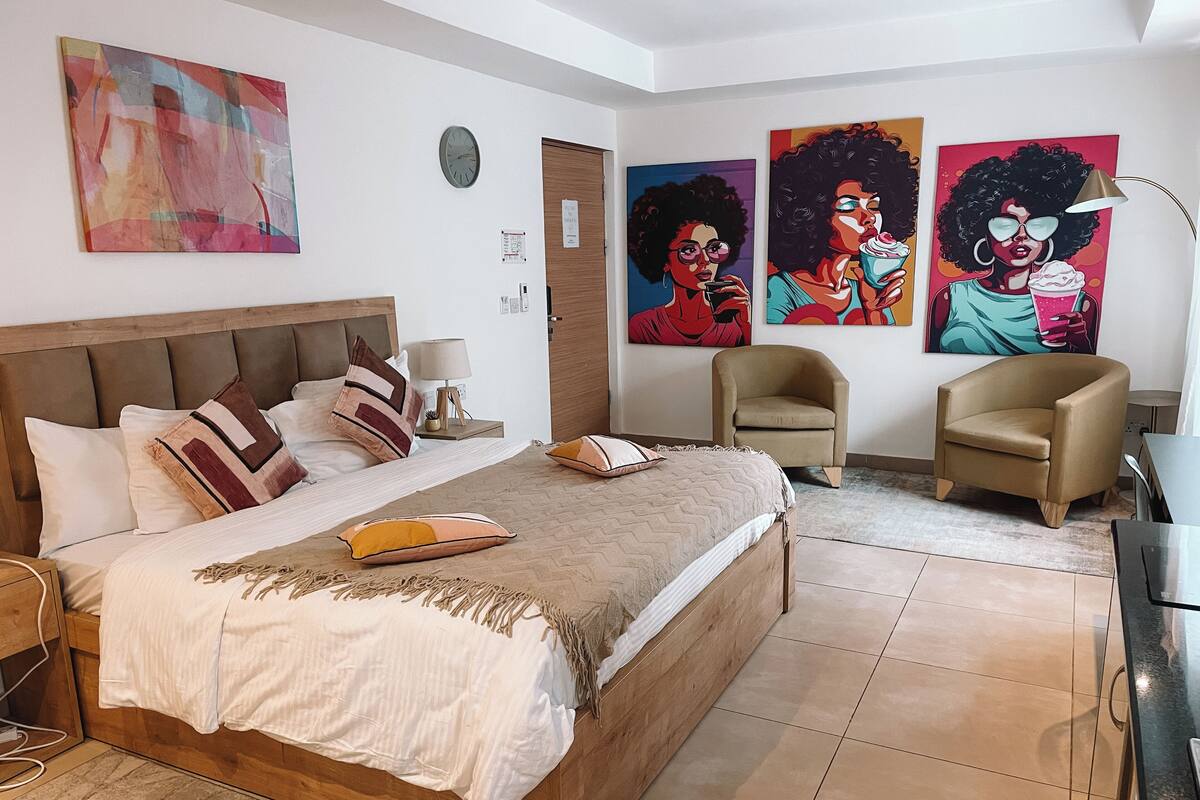 Une chambre à coucher avec un grand lit, deux fauteuils, un bureau et des œuvres d’art accrochées aux murs.