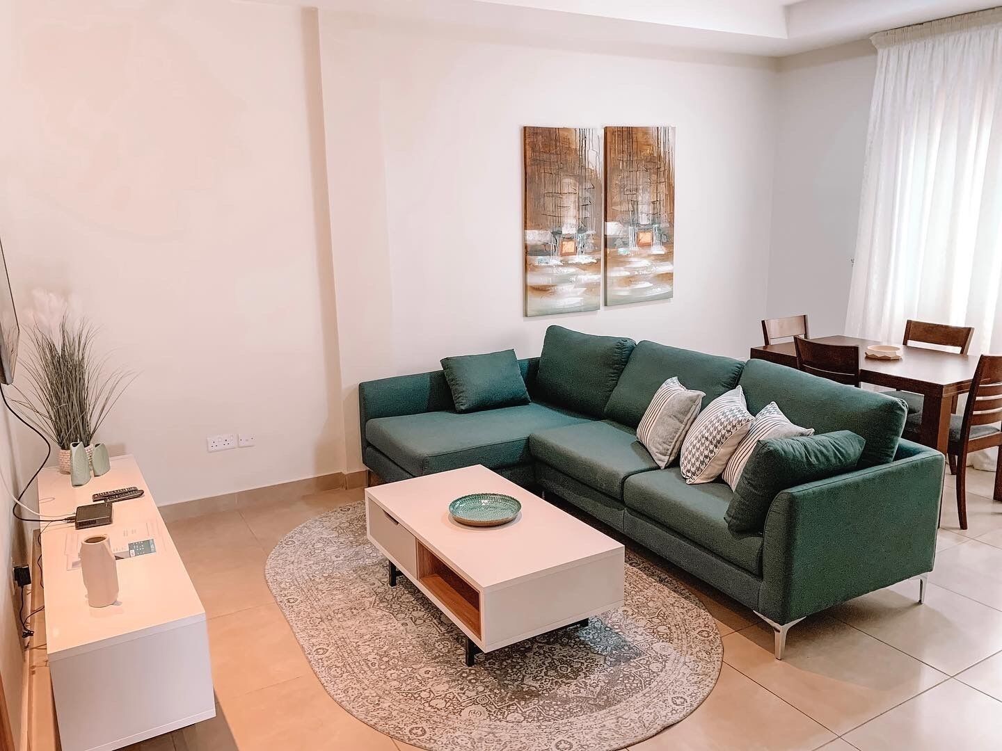 A modern living room with a green sofa, a white coffee table, and two abstract paintings on the wall.