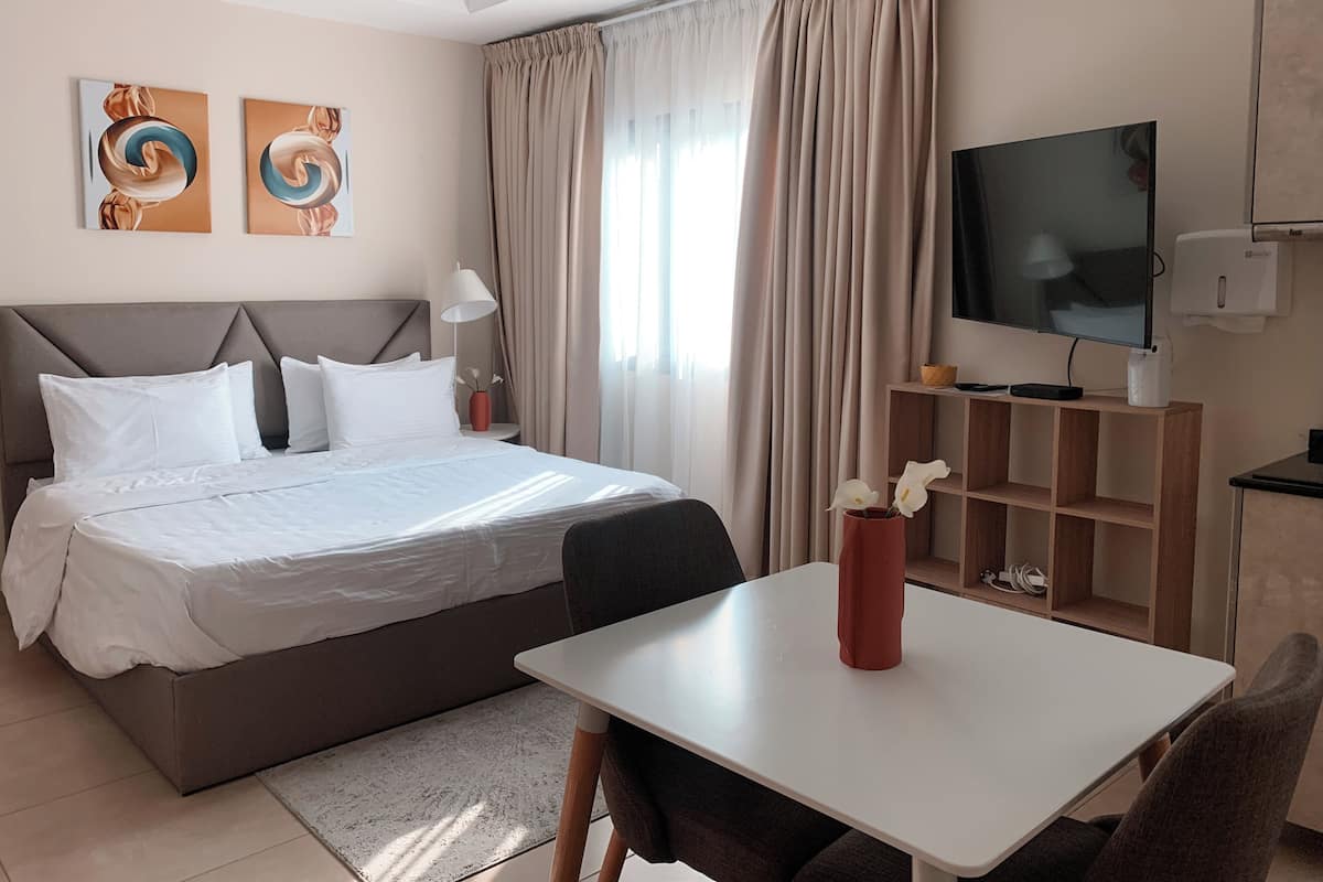 Une chambre d’hôtel moderne, dotée d’un grand lit, d’une télévision, d’un bureau et d’une petite table sur laquelle est posé un vase.