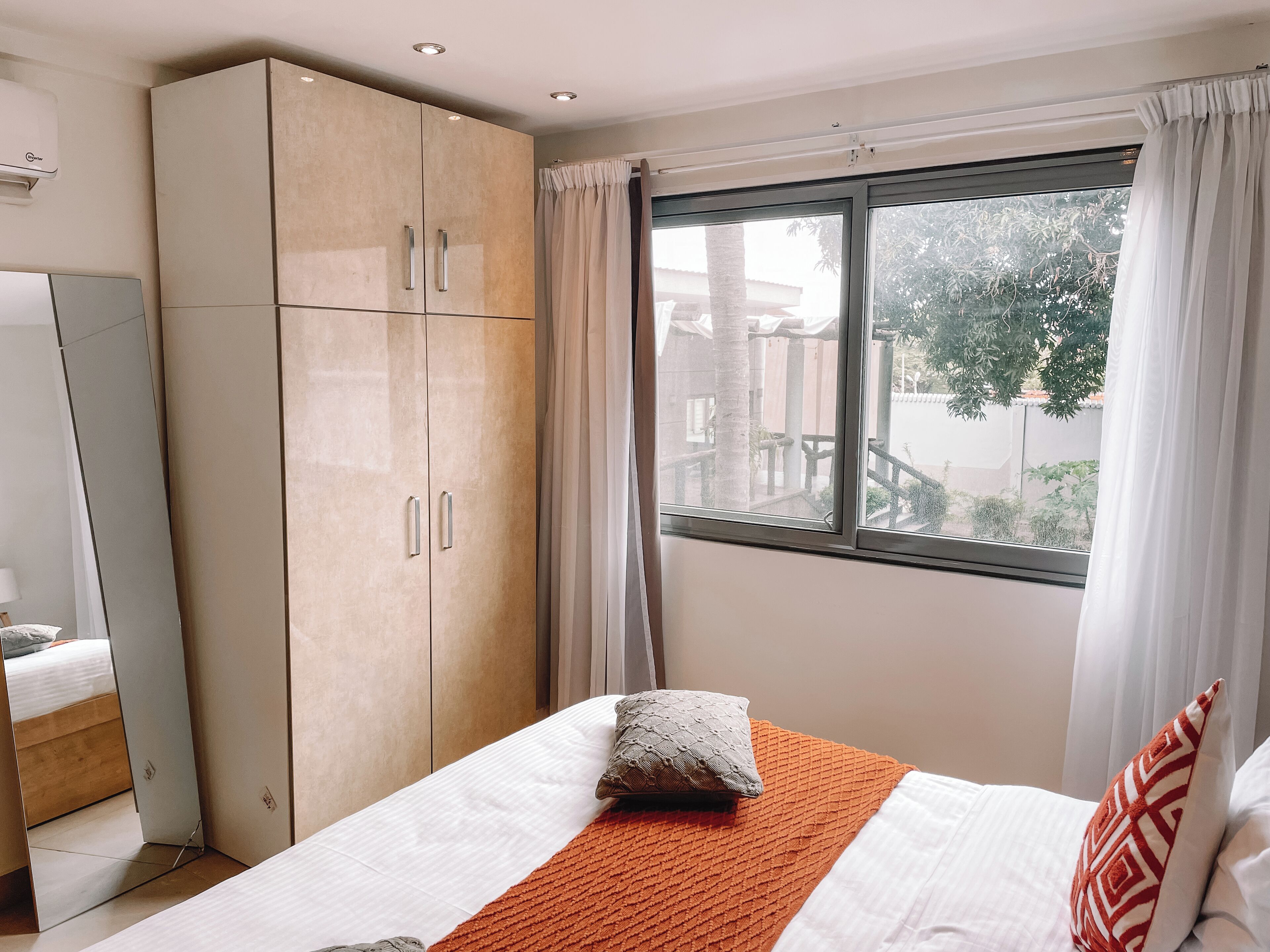 A bedroom with a bed, a wardrobe, a window with curtains, and a view of the outside.