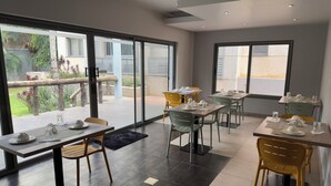 A modern dining area with multiple tables and chairs, large windows offering a view of the outdoors, and a clean, contemporary interior design. - Sky Suites Airport (Accra)
