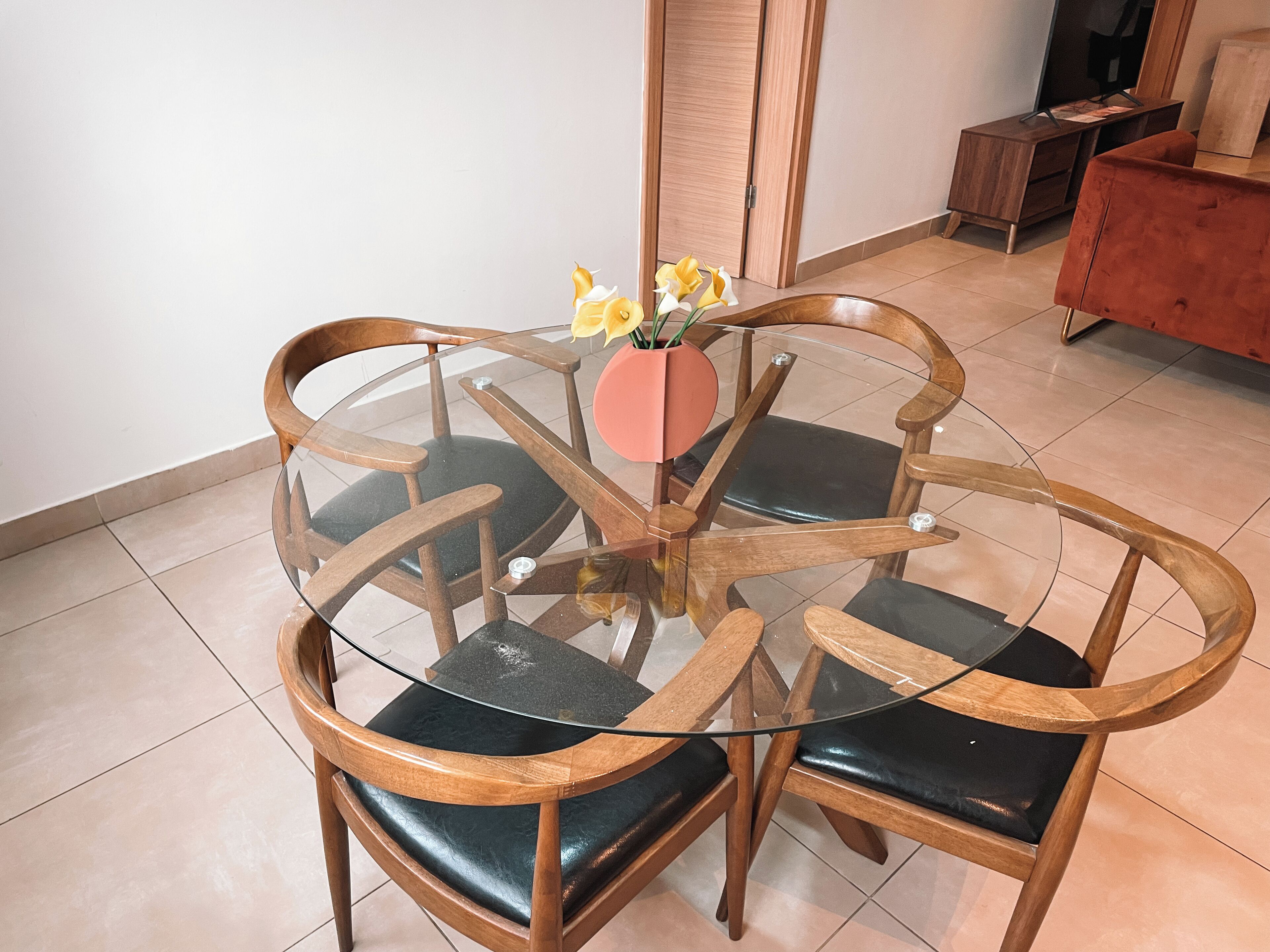 Een ronde glazen tafel met houten stoelen en een vaas met bloemen.