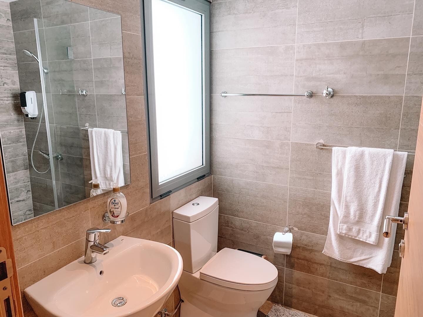 Une salle de bain moderne avec une douche à parois de verre, un lavabo blanc, des toilettes et un grand miroir.
