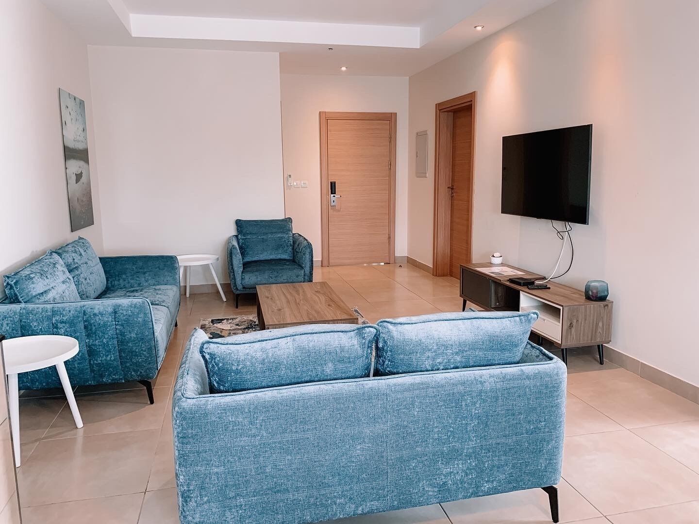 A modern living room with a blue sofa set, a wooden coffee table, a TV, and a small side table.