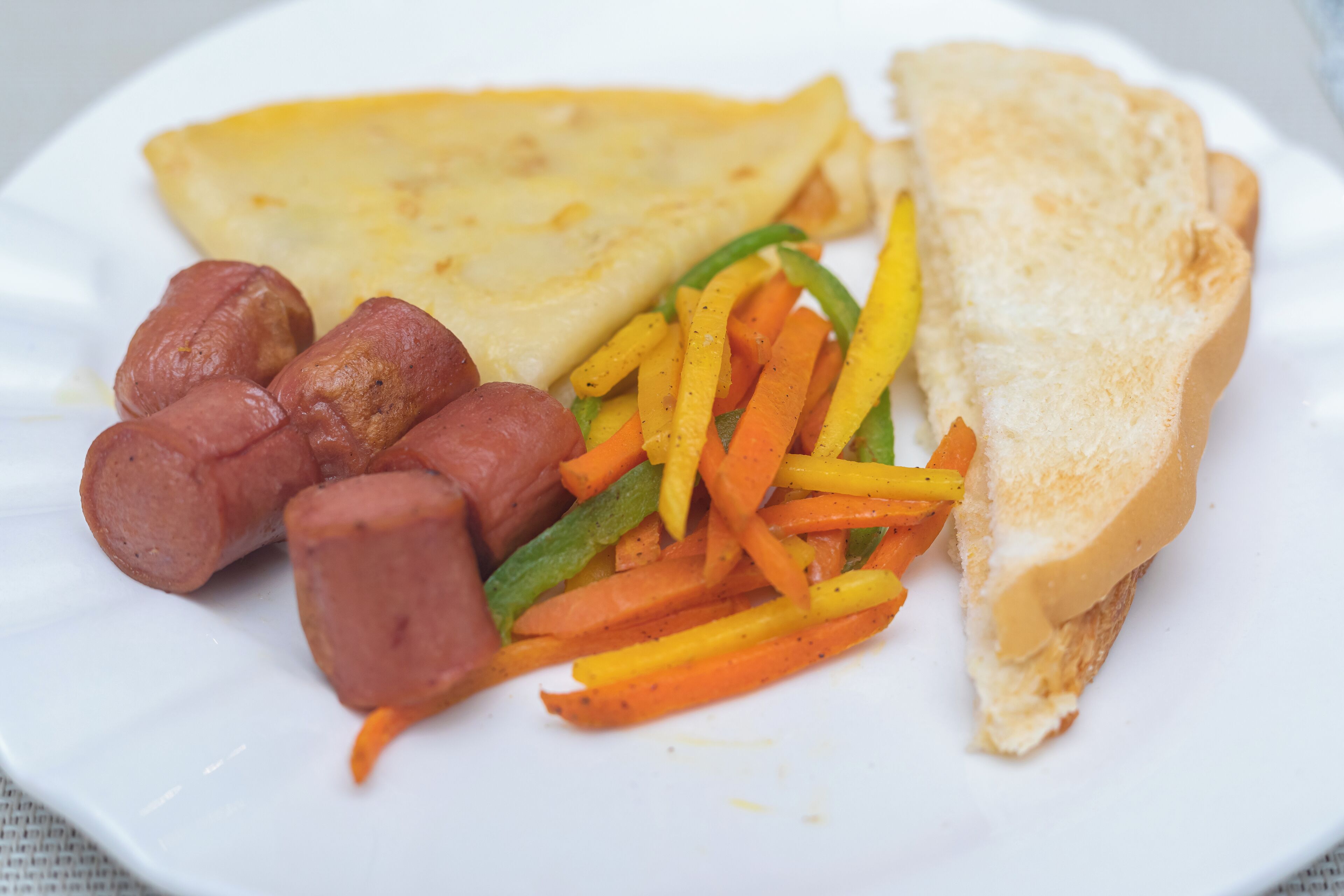Un piatto con un panino, salsiccia e verdure a fette.