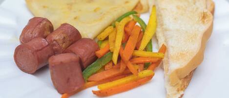 A plate with a sandwich, sausage, and sliced vegetables.