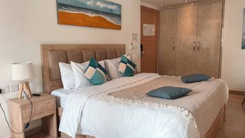 A bedroom with a bed, nightstand, lamp, and a painting of a beach scene.