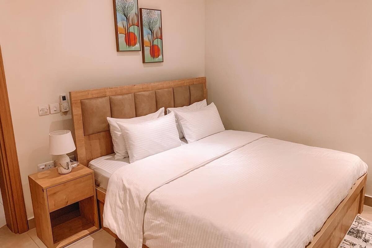 Un lit bien fait, avec du linge de lit blanc, une tête de lit en bois et une table de chevet avec une lampe.