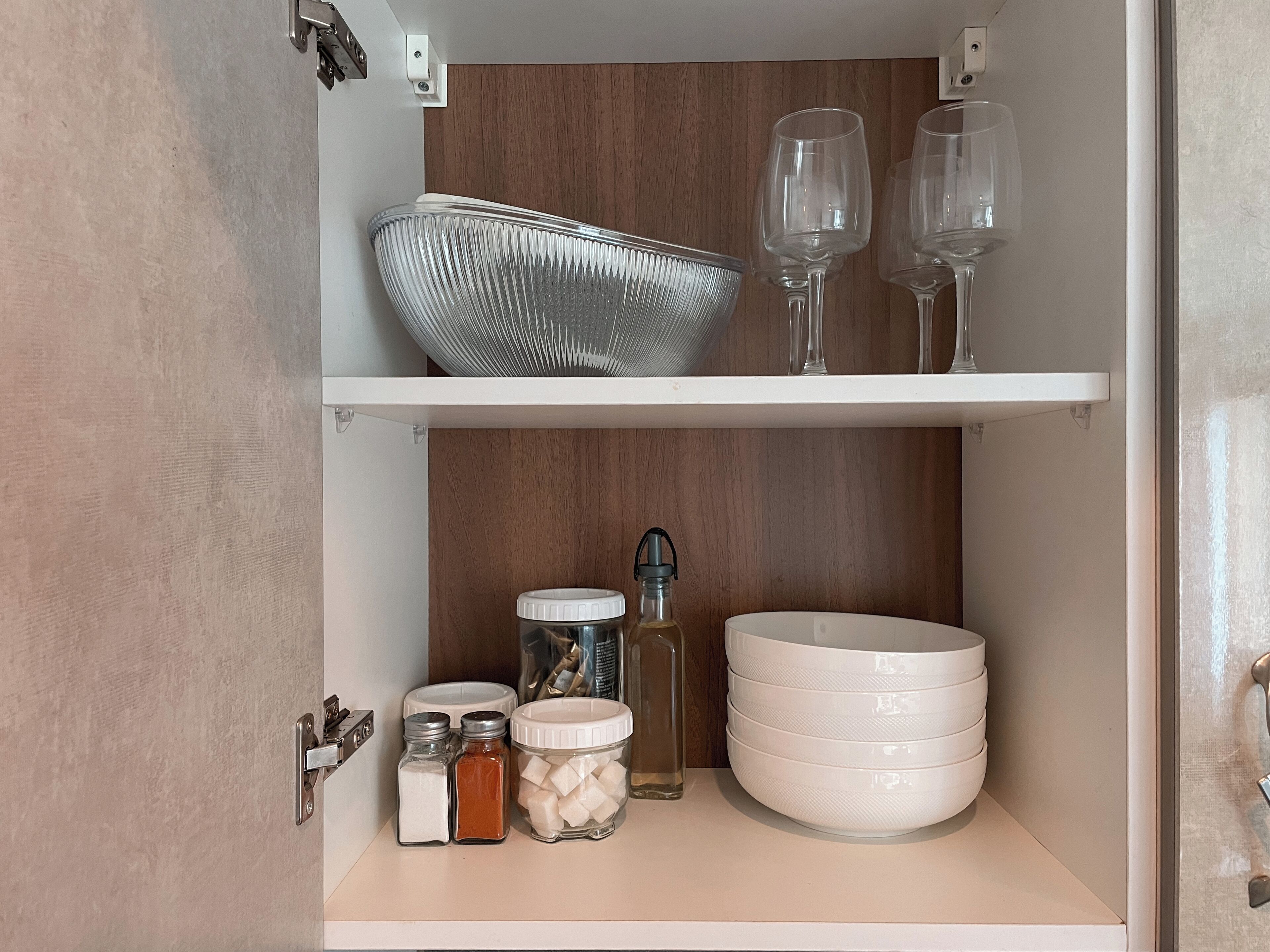 A kitchen pantry with shelves holding a glass bowl, wine glasses, jars of sugar, and salt.