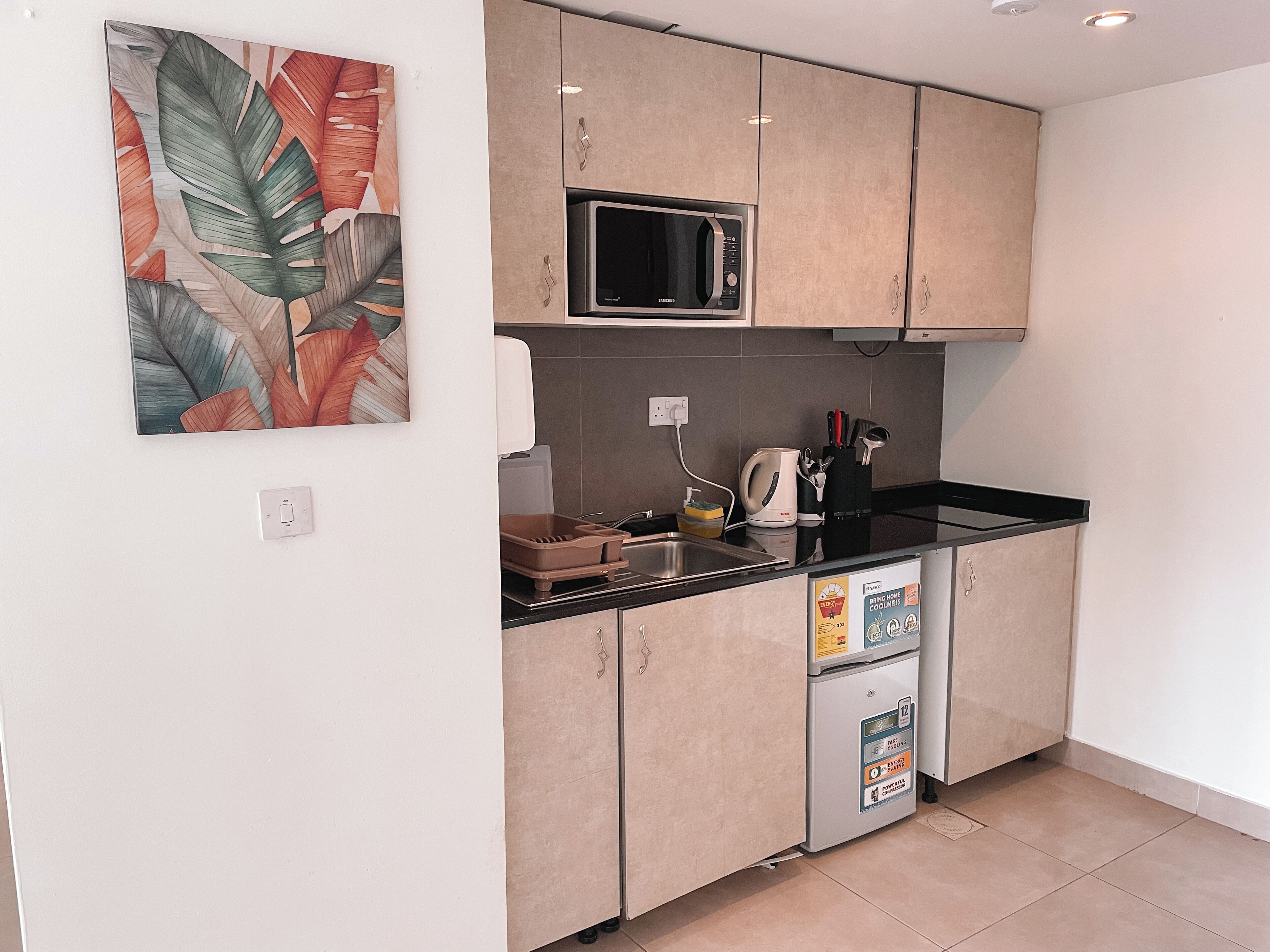 Una cocina compacta con microondas, hervidor y un refrigerador pequeño.