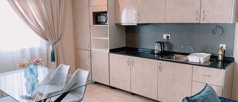 A modern kitchen with a glass dining table, light-colored cabinets, and a blue sofa.
